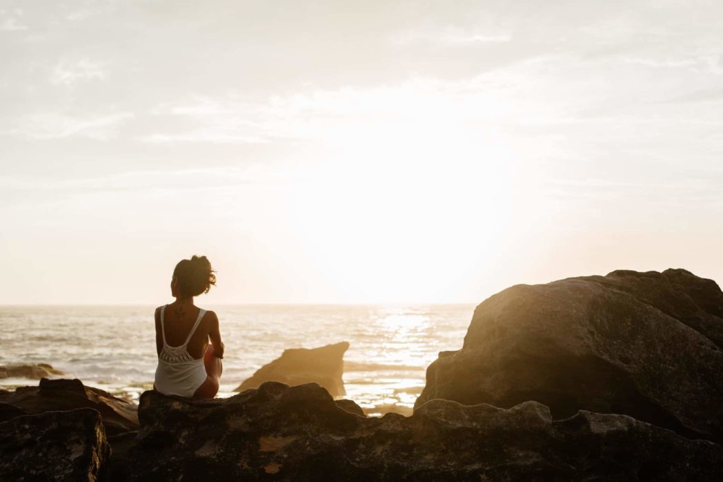 Self Development - woman sitting on rocks in front of the ocean