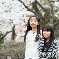 two girls standing behind brown tree with white leaves