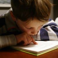 boy in gray and red hoodie reading book