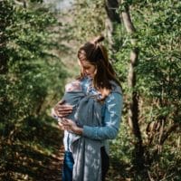 woman carrying child while standing near trees at daytime