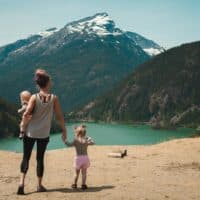 A mother with two children enjoys a scenic mountain and lake view during a sunny outdoor hike.