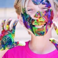 A joyful child with vibrant face paint and hands, expressing happiness and creativity.