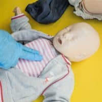 A person demonstrates infant CPR on a manikin, highlighting first aid techniques.