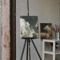 Cozy art studio featuring cloud paintings on easels and paintbrushes, captured indoors.