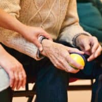 An elderly person receives support from a caregiver, holding hands indoors, showcasing compassion.