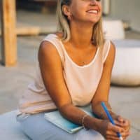Smiling woman enjoying a peaceful moment with a notebook outdoors, symbolizing relaxation and mindfulness.