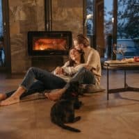 A loving couple relaxes by the fireplace with their dog, enjoying a cozy indoor atmosphere.