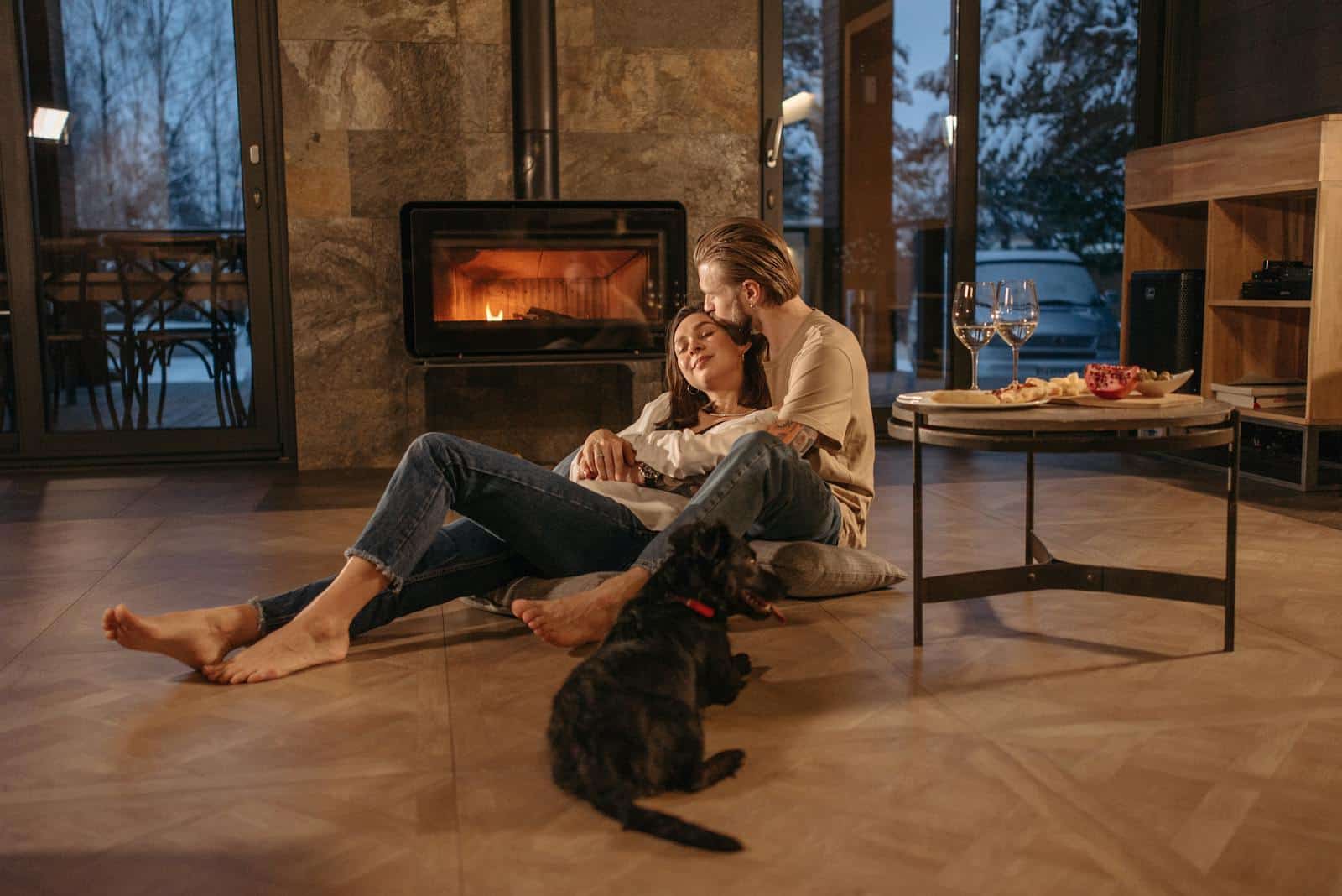 A loving couple relaxes by the fireplace with their dog, enjoying a cozy indoor atmosphere.