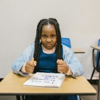 A young girl sits at a desk with a determined expression, promoting anti-bullying.