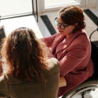 Woman in Red Sweater Wearing Black Framed Eyeglasses Sitting on Wheelchair