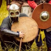 Medieval warriors in armor at a reenactment event, showcasing shields and helmets.