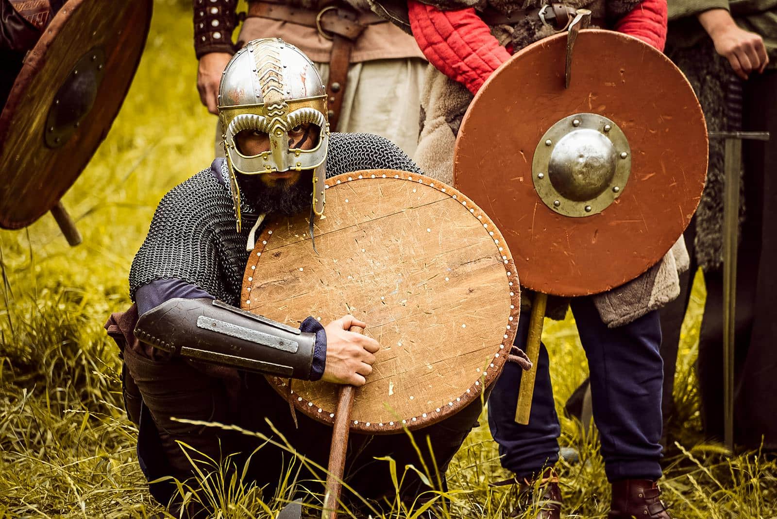 Medieval warriors in armor at a reenactment event, showcasing shields and helmets.