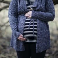 Pregnant woman in striped shirt and cozy sweater outdoors, embracing motherhood.