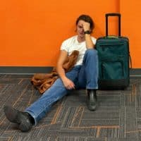 Man sitting on floor with luggage, looking tired.