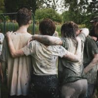 Group of teenagers bonding in a muddy team-building exercise outdoors.