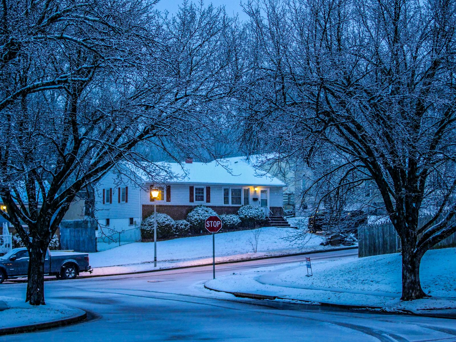 Idyllic snowy suburban street capturing warm house lights and serene wintertime atmosphere at twilight.